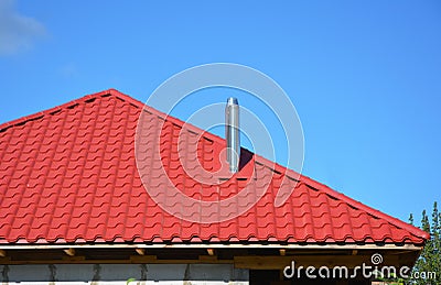 Roofing Construction. New red metal tiled roof with steel chimney house roofing construction exterior without rain gutter system. Stock Photo