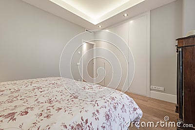 Room with a double bed with a patterned quilt, a built-in wardrobe with four smooth wooden doors, a balcony and wooden floors Stock Photo