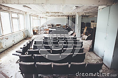 Room with raws of chairs in abandoned and ruined industrial factory, creepy aged building after war, no people Stock Photo