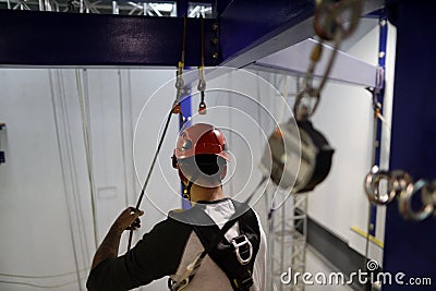 Rope access abseiler wearing red safety fall protection helmet working at heights attached an inertia reel shock absorber lanyard Editorial Stock Photo