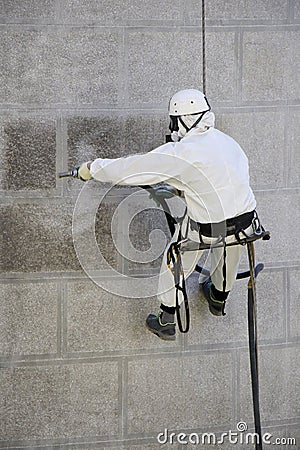 Worker wearing a protective gear cleaning a stone faceade in rope access Stock Photo