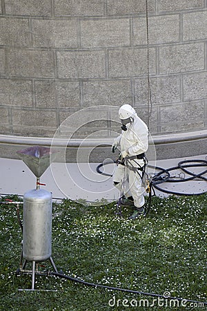 Worker wearing a protective gear cleaning a stone faceade in rope access Stock Photo