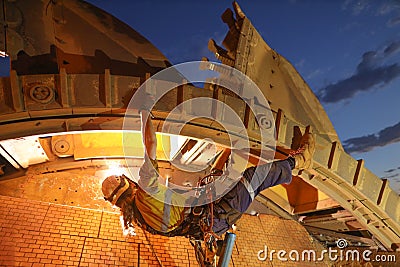 Rope access welder maintenance abseiler wearing fall safety body harness helmet protection hanging upside down welding repairing Stock Photo