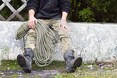Rope on the background of an old tram stop with a man in his hands. camouflage pants, black army boots. Retro wooden construction Stock Photo