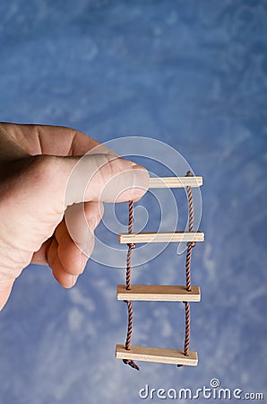 Rope ladder toy holding in adult hand on blue background. Climbing for success imaginations. Stock Photo