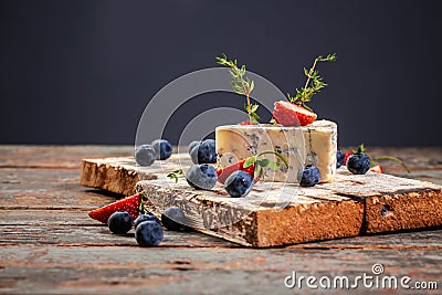 Roquefort, French blue cheese with mold on a wooden surface, served with blueberry and strawberry Stock Photo