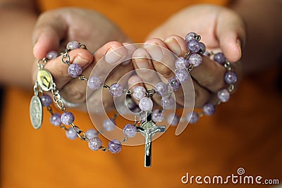 Rosary in hand. Young junior lady holding rosary with open hand. Female hands holding a rosary with Jesus Christ Cross or Crucifix Stock Photo