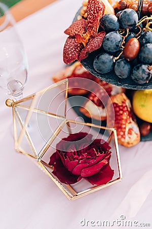 Rose in a case, a box for rings, on a table with a whatnot with grapes and pomegranates at a wedding. Stock Photo