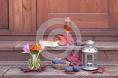 Rose champagne, book, lantern, figs, helenium and and autumn crocuses on steps of rustic wooden ladder Stock Photo