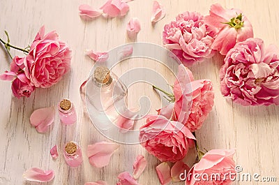 Rose water in glass bottle and pink flowers with petals on white wooden background. SPA or aromatherapy concept Stock Photo