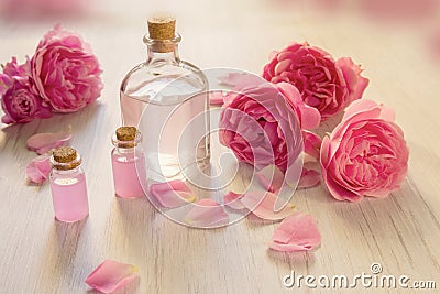 Rose water or oil bottles on wooden white background. Beautiful pink flowers and petals, aromatherapy and SPA concept Stock Photo