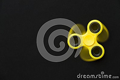 Rotating yellow fidget spinner device on black background. Top view. Playing with a yellow hand spinner fidget toy Stock Photo
