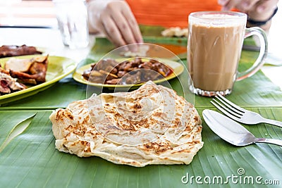 Roti canai or paratha served on banana leaf, with mutton curry and fried chicken, and popular teh tarik Stock Photo