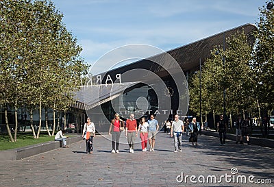 Family group of people walking through pedestrian area in summer sunshine. Modern building and trees in background Editorial Stock Photo