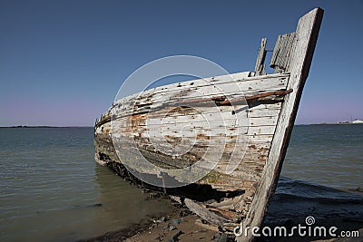 Rotting holed hulk of old wooden fishing boat beached Stock Photo