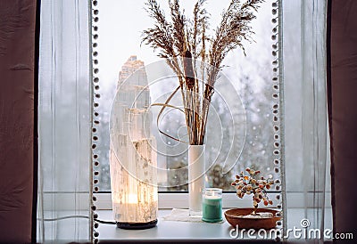 Rough big selenite crystal tower lamp illuminated on home window sill, spiritual home decor accent. Stock Photo