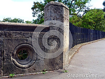 Rough gray stone railing olong public street and black steel fence beyond Stock Photo