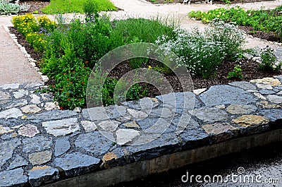 Rough-hewn limestone stones on the paving of a path in a park above a regularly shaped pond. tralk beds around. gray and brown mix Stock Photo