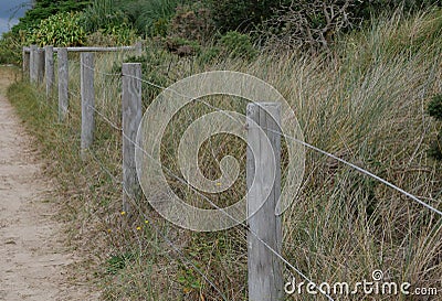 Rough wood and wire fence alongside sandy path and coarse grass Stock Photo