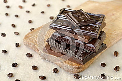 Roughly broken pieces of chocolate are stacked on a wooden board, coffee beans are scattered around Stock Photo