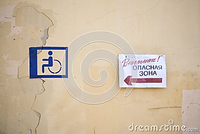Roughly drawn sign of a disabled person on a yellow wall. The plate with the inscription in Russian. Stock Photo