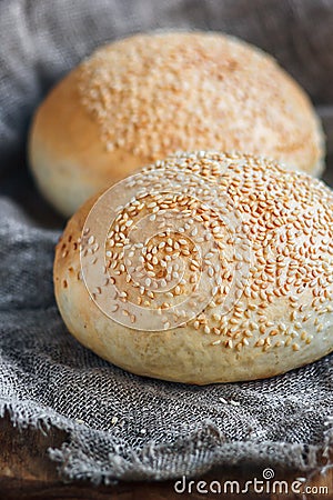 Round bun, sesame bun, bread rolls. Tasty burger bread with sesame on wooden, burlap background. Freshly baked hamburger buns. Top Stock Photo