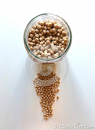 A round glass jar with chickpeas inside and in front of a set of more chickpeas on a white table Stock Photo