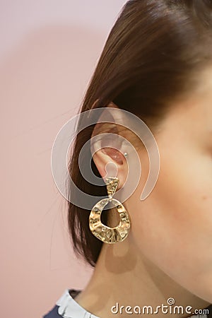 round gold earrings on the ear of a brunette on a pink pastel background Stock Photo