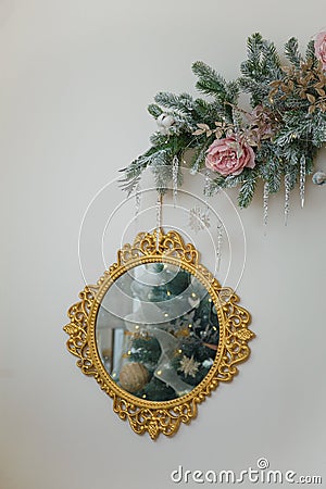 Round golden mirror with decorated Christmas tree reflection. Snowy fir branches with icycles, icy roses hanging on wall. Copy Stock Photo