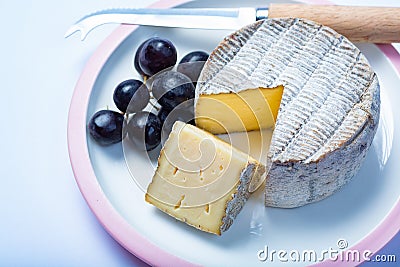 Round mature French Tomme cheese with one cutted piece close up isolated Stock Photo