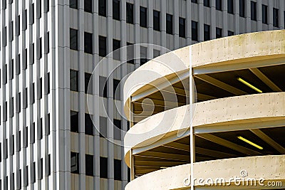 Round, metal clad parking garage in faded yellow backed by monochrome skyscraper Stock Photo