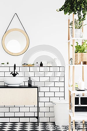 Round mirror above white washbasin in modern bathroom interior with plants. Real photo Stock Photo