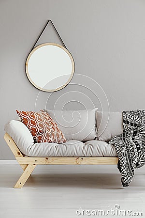 Round mirror hanging on the wall in bright living room interior with light grey sofa with cushion and blanket in real photo Stock Photo