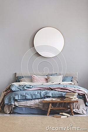 Round mirror in wooden frame on grey wall of elegant bedroom interior with comfortable bed with pastel, blue and pink bedding Stock Photo