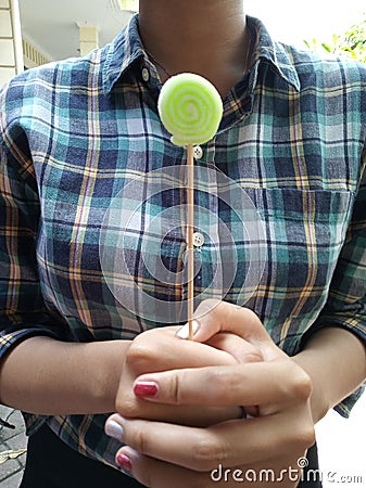 A girl standing holding a green candy stick. Stock Photo