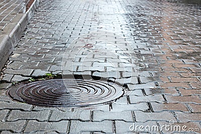 Round steel sewer manhole on wet cobblestone road Stock Photo