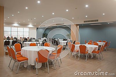 Round table with a white tablecloth, orange and black chairs in a modern restaurant or banquet room of a luxury hotel. Catering Editorial Stock Photo