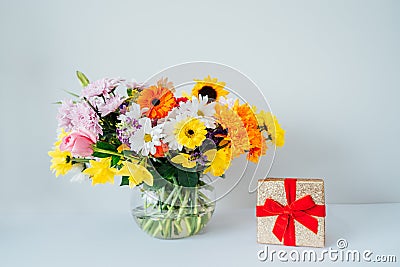 Round Vase with huge multicolor various mixed flower bouquet and shining golden gift box with red velvet ribbon Stock Photo
