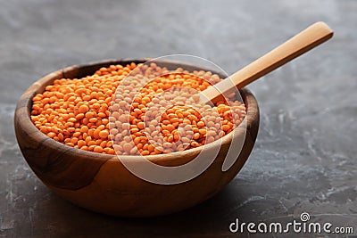A round wooden bowl filled with red lentils with a wooden spoon stands on a dark background Stock Photo
