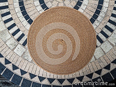 A round woven placemat on a tiled table surface Stock Photo