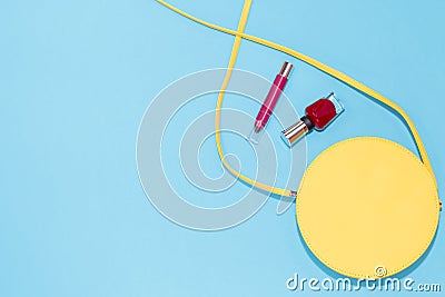 Round yellow purse, red nail polish, red lipstick on a pastel blue background. Stock Photo