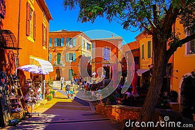 View beyond tree on street with bright yellow, ochre and red French mediterranean houses against blue sky Editorial Stock Photo