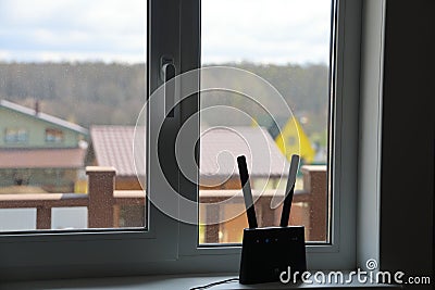 The router is on the windowsill, the country houses are visible in the window, remote work, freelance Stock Photo