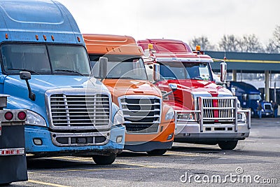Row of different big rigs semi trucks on truck stop parking lot waiting for continuation of the road routes Stock Photo