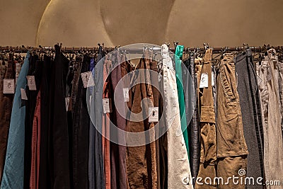 Row of earth tone colour fabric jeans or denim trousers and slacks hang on hanger. Stock Photo