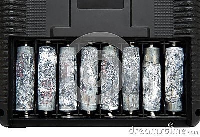 A row of eight unwrapped and heavily oxidized AA batteries inside the battery compartment of an electronic device Stock Photo