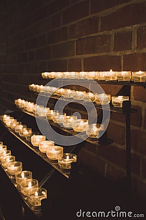 Row of glowing candles in church. Candles with flame on dark background. Faith and religion concept. Candles in catholic church. Stock Photo