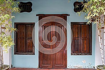 Row house facade background show dark wooden entrance door and windows with steel rod on light blue wall with bamboo plant pot Stock Photo