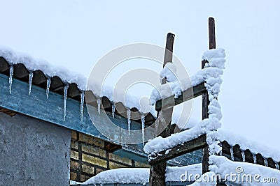 A row of icicles on a slate roof and a wooden ladder under the snow Stock Photo