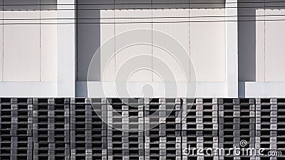Many stacked plastic pallets outside of white warehouse building Stock Photo